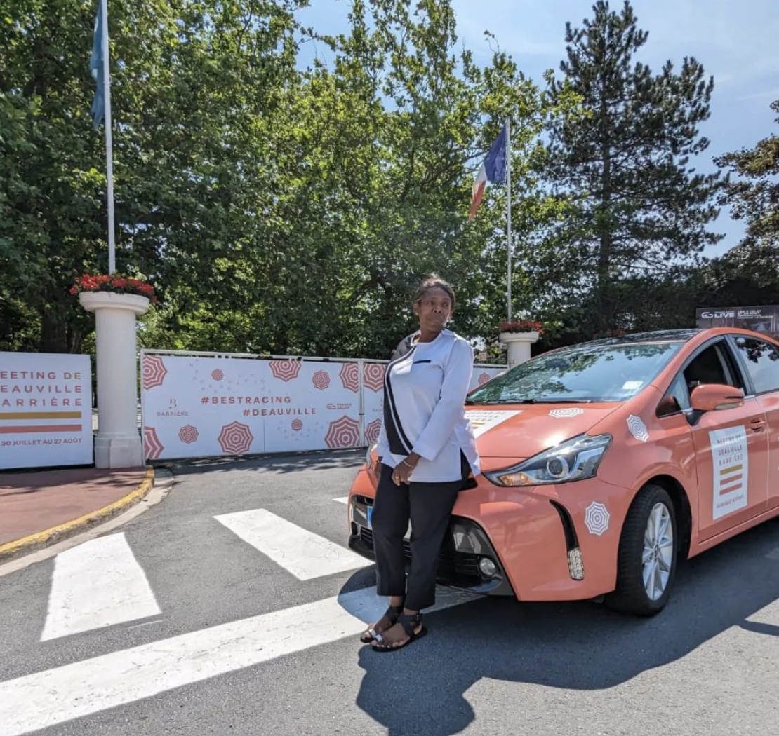 Chauffeur posant à côté d'un véhicule Toyota hybride orange et blanc.